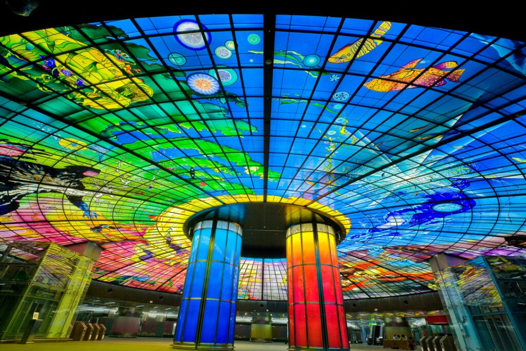 A vibrant and colorful stained glass ceiling with various intricate designs, enhanced by multiple pillars in a large indoor space.