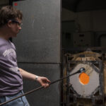 man blowing glass at a glory hole