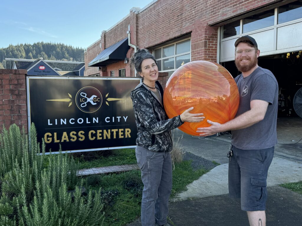 two people holding a large glass sculpture outside